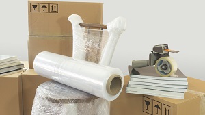 Moving scene with a roll of plastic to pack on a chair wrapped in plastic with closed cardboard boxes, books and masking tape on white background, moving guide